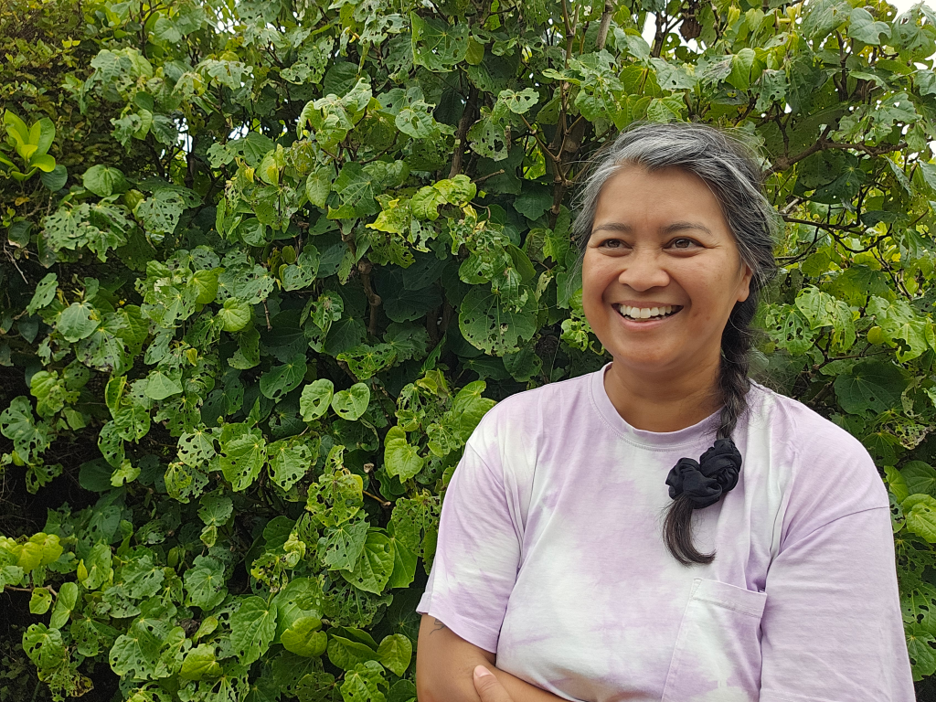 Middle aged asian woman in front of a kawakawa bush looking off camera